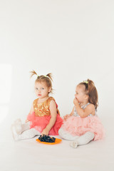 two little girls eating grapes sitting on the floor on a white background