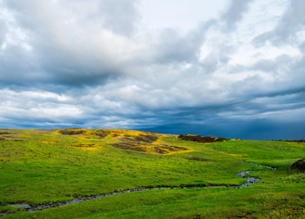Fototapeta na wymiar Storm clouds passing over a tranquil scene of a creek in a beautiful green meadow on Table Mountain in Northern California.