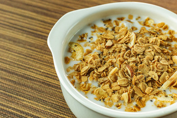 Morning food almond flakes  and milk in white bowl on wood table.