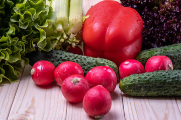 fresh vegetables on a light wooden table, paprika, celery, leaves of lettuce, cucumbers and radishes