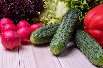 fresh vegetables on a light wooden table, paprika, celery, leaves of lettuce, cucumbers and radishes