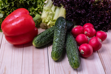 fresh vegetables on a light wooden table, paprika, celery, leaves of lettuce, cucumbers and radishes