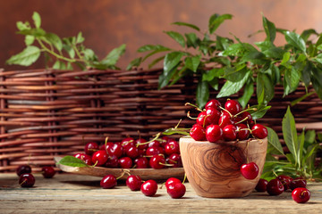 Red sweet cherry in a wooden bowl on a wooden table in garden.