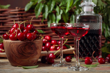 Cherry liquor and red cherries in a wooden bowl on a wooden table in garden.