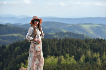 Beautiful, young girl tourist in a pink dress and hat against the sky and mountains in the Schwarzwald, Germany