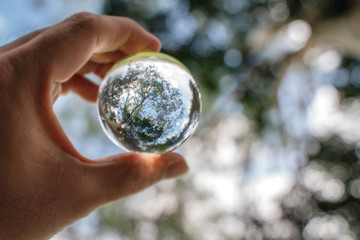 Reflection of blue sky, white clouds and trees in a glass ball in holding hand - obrazy, fototapety, plakaty