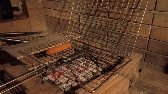 Handheld Shot of Man Placing Sausages into a Grilling Basket on a Charcoal BBQ at Night