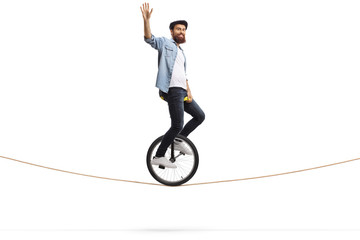 Bearded young man riding a unicycle on a rope and waving © Ljupco Smokovski