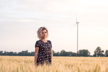 young tanned curly haired woman in dress is happy to be on the field of ripened wheat, sunset time