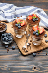 Fototapeta na wymiar Classic tiramisu dessert with blueberries and strawberries in a glass on wooden background