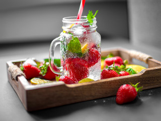 Strawberry fruit, mint leaves, lime and lemon halves on a vintage wooden tray. Mojito mix on the rustic wooden salver. Lemonade, beverage or cocktail with ice, lemon, strawberries and mint.