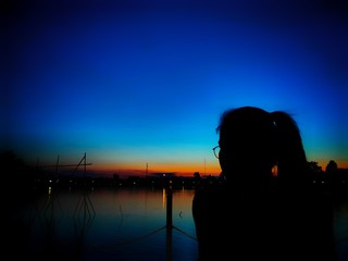 Fototapeta premium Asian woman is sitting Along the water at dusk, with the sunset 