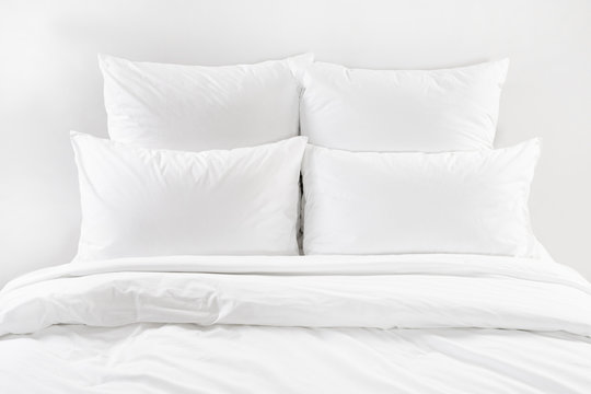White bed isolated, four white pillows and duvet on a bed