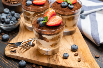 Classic tiramisu dessert with blueberries and strawberries in a glass on wooden background