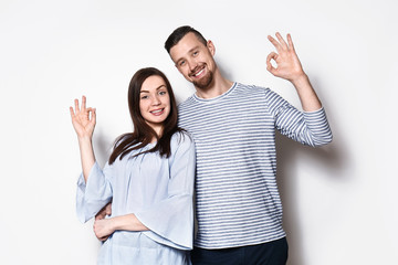 Happy young couple showing OK gesture on light background