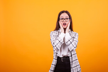 Beautiful portrait of shocked adolescent girl with eye glasses over yellow background in studio