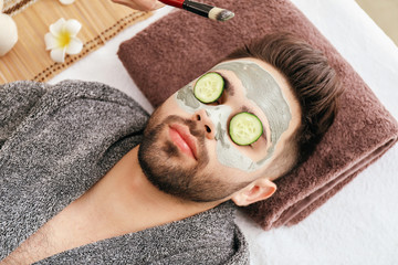 Young man with clay mask on his face in beauty salon