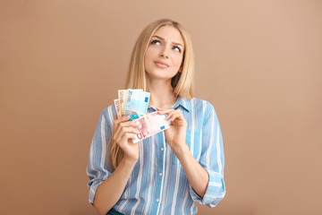 Thoughtful young woman with money on color background