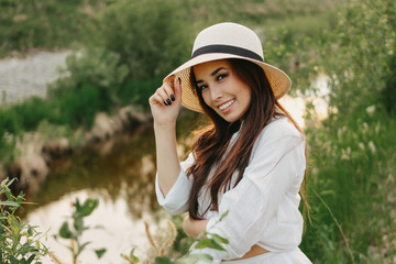 Beautiful carefree long hair asian girl in white clothesand straw hat  on river side in the grass...