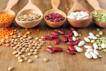 Spoons with different legumes on wooden background