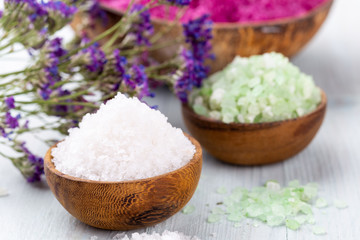 Sea salt in bowl, aroma oil in bottles, Wellness and flowers on grey textured background and flowers on vintage wooden background. Selective focus.