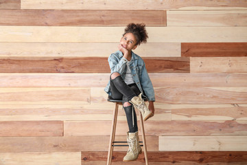 Stylish African-American girl in jeans clothes near wooden wall