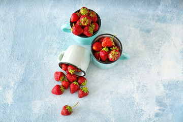 Mugs with ripe red strawberry on color table