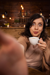 Beautiful young woman smiling and using smarthphone to make a self-portrait in a coffee shop