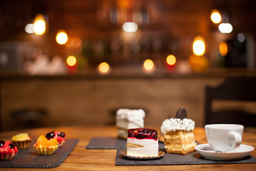Delicious diffrerent cakes with a cup of tasty coffee over a wooden table in a coffee shop