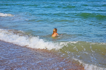 little girl swims alone in the sea with a wave