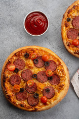 Tasty pepperoni pizza and cooking ingredients tomatoes basil on grey concrete background. Top view of hot pepperoni pizza. With copy space for text.