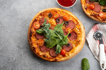 Tasty pepperoni pizza and cooking ingredients tomatoes basil on grey concrete background. Top view of hot pepperoni pizza. With copy space for text.