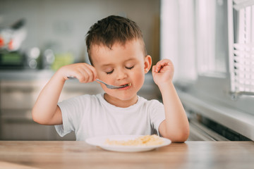 a child in the kitchen during the day eating pasta in a spiral in a white t-shirt