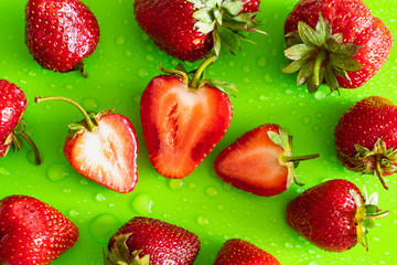 Red sweet ripe strawberry berry on green matte background with water drops