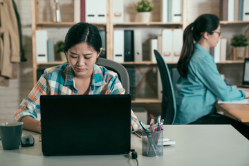 skillful asian female executive thinking over working schedule for employee writing report into notebook while using laptop computer and wireless connection in coworking space. two women colleagues.
