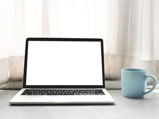 Fototapeta premium White screen laptop computer, blue coffee mug on gray wooden table.