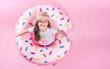 A little child girl lying on a donut inflatable circle. Pink background. Top view. Summer concept.