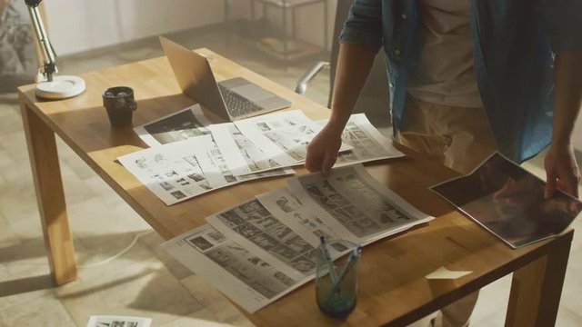 Creative Designer Works on a Storyboard, Looks at His Sketches and Concepts, Choosing the Best Drawings for His Project. Video Editing, Comics Compilation, Application UI or Game Plot. High Angle