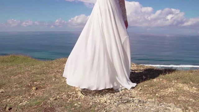Pretty young bride on cliff white dress fluttering in the wind