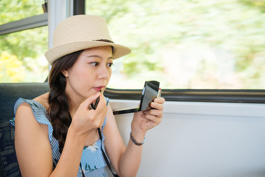 Beautiful Woman Traveler Repairing Makeup In Train Subway By Window. Young Girl Tourists Doing Make Up Lipsticks With Cosmetic Looking In Mirror Sitting On Metro Taking Commute While Traveling.