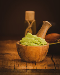 Fresh guacamole in wooden bowl with ingredients on rustic table.