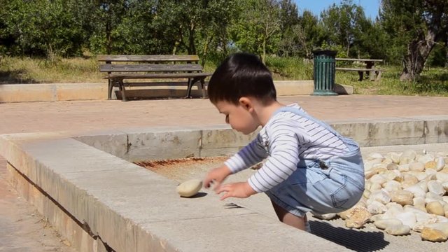 Cute two years old boy playing with rocks in the park