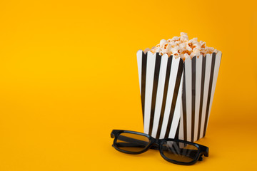 Popcorn in paper bag stand on yellow background top view fnd black 3d glasses