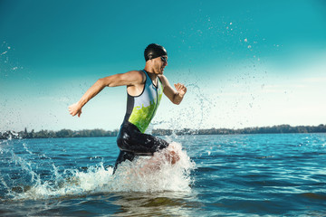 Professional triathlete swimming in river's open water. Man wearing swim equipment practicing triathlon on the beach in summer's day. Concept of healthy lifestyle, sport, action, motion and movement. - obrazy, fototapety, plakaty