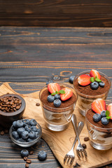 Classic tiramisu dessert with blueberries and strawberries in a glass on wooden background
