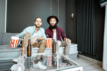 Two male friends watching football match, cheering up for the sports team while sitting with drinks...