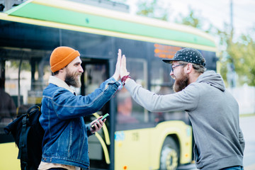 Cute attractive handsome guy wearing casual shirt and glasses outside holding smartphone smiling showing high five hey hello hi sign outdoor over bus on background