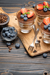 Classic tiramisu dessert with blueberries and strawberries in a glass on wooden background