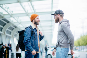 Two cute attractive handsome men wearing casualclothes and glasses outside meeting talking smiling showing outdoor over bus stop on background.