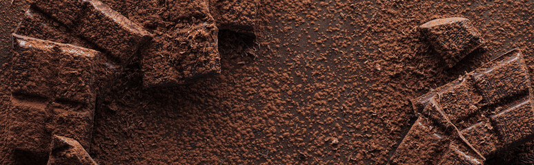Panoramic shot of pieces of chocolate with liquid chocolate and cocoa powder on metal background